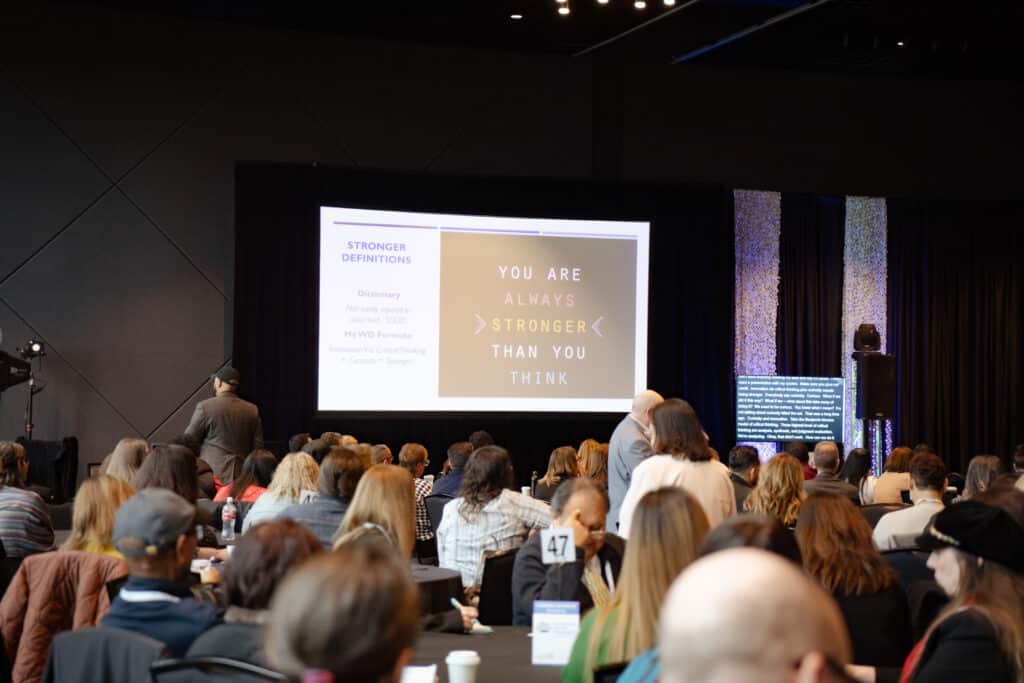 An event space full of people with a projector screen in the background that says "You are always stronger than you think."