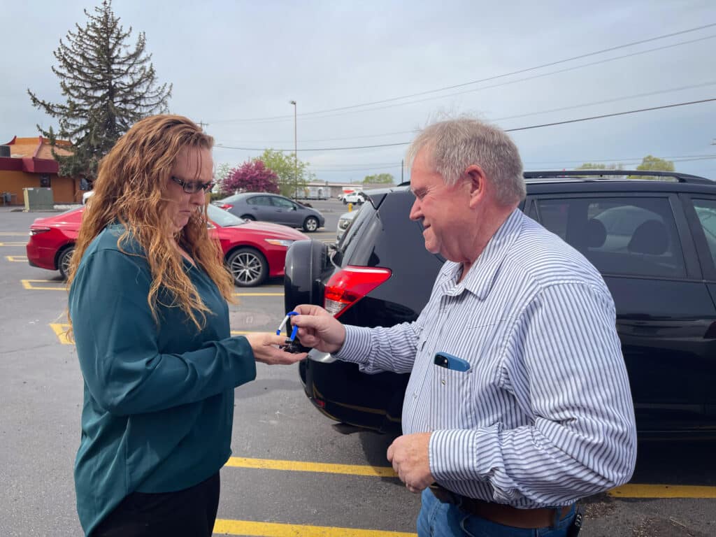 A man in a striped shirt hands over the car keys to a woman in a blue shirt.