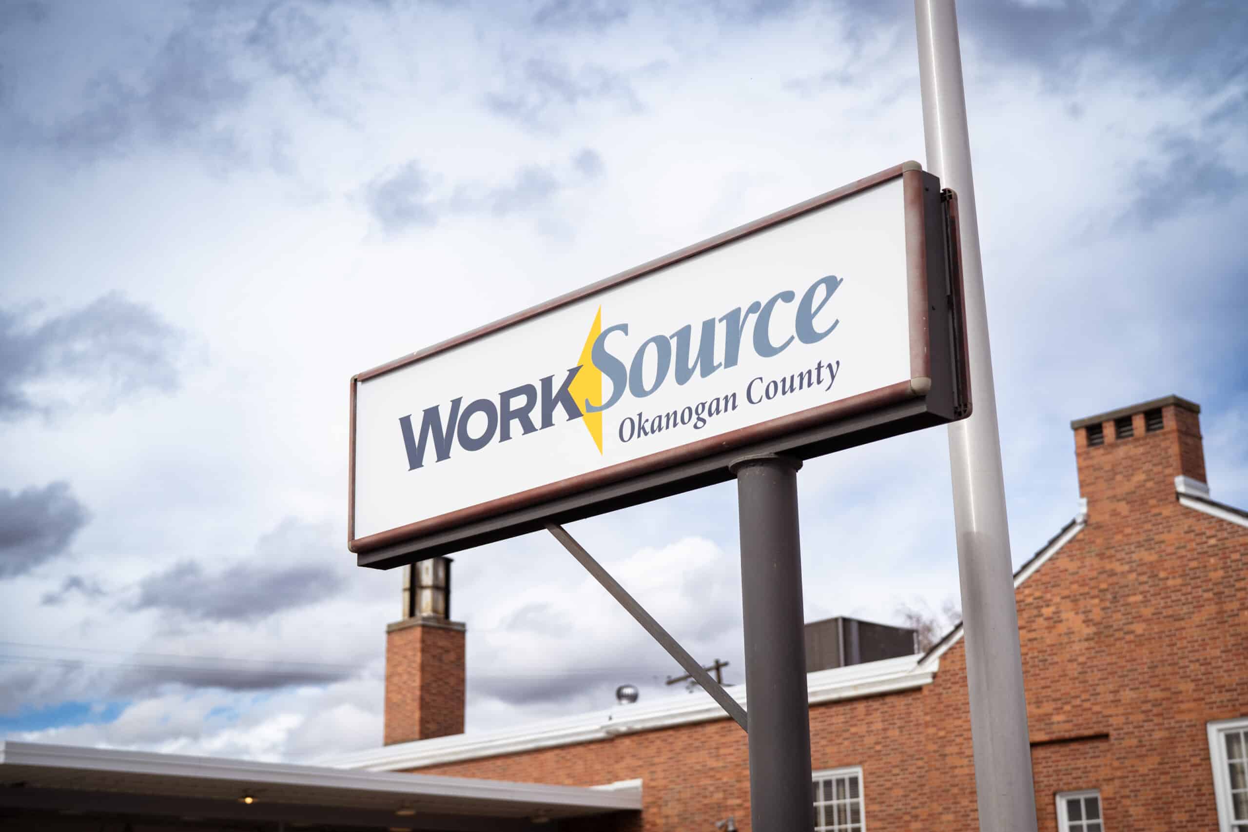 A white sign with the word WorkSource against a blue sky with gray and white clouds.