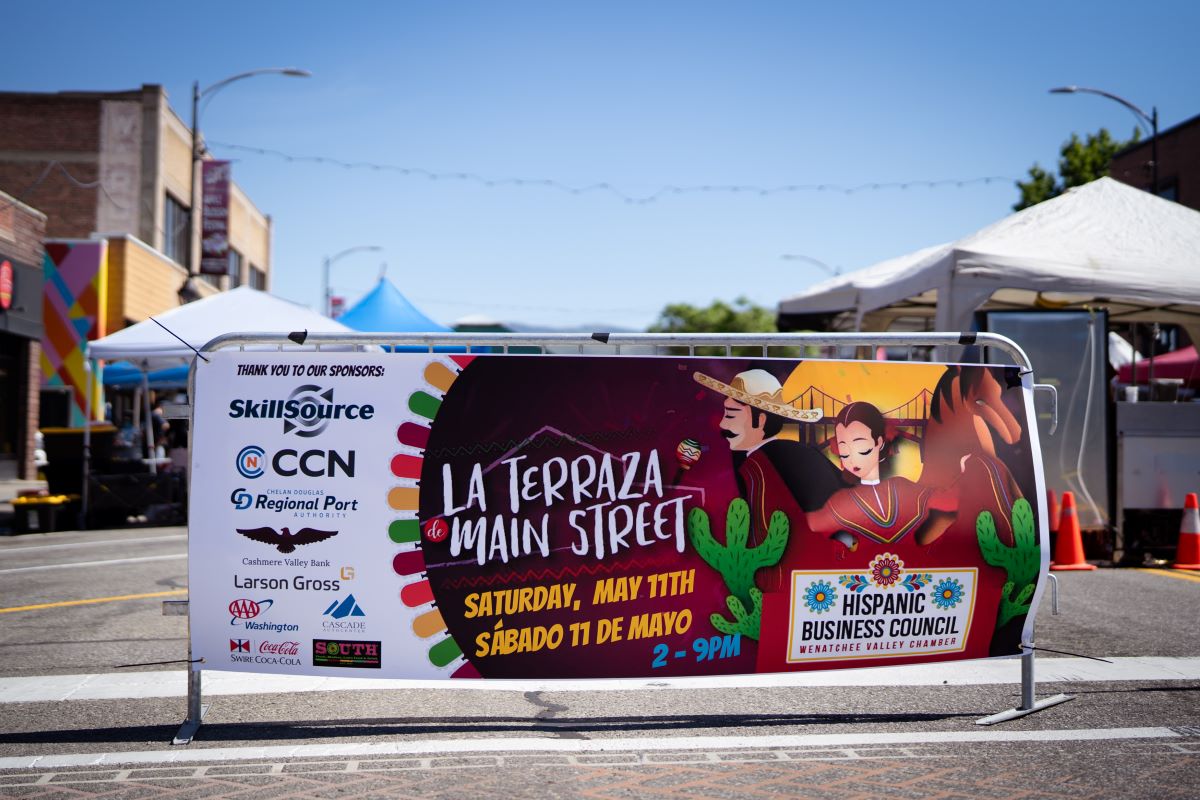 A banner that reads La Terraza de Main Street sits at the entrance to a street festival with blue sky in the background.