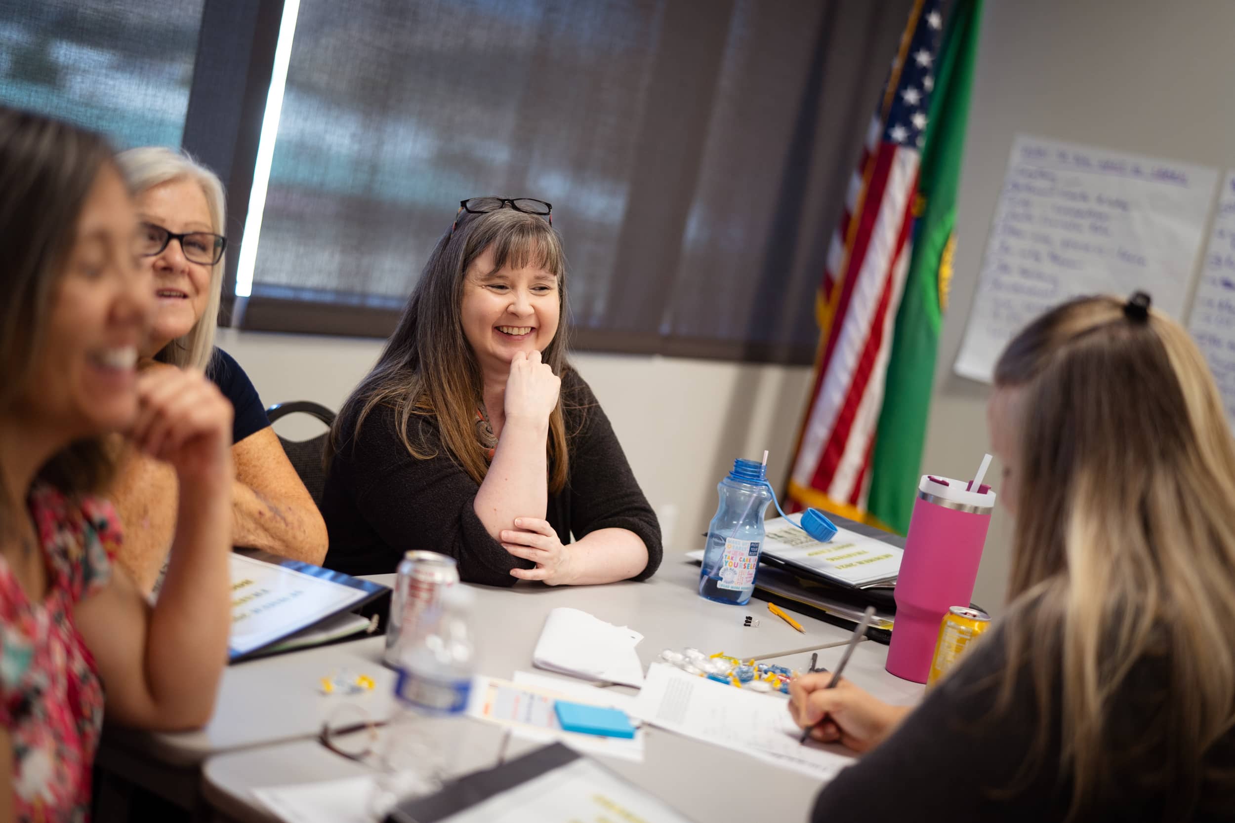 A smiling woman seated with three other people at a table with papers and sticky notes on it.
