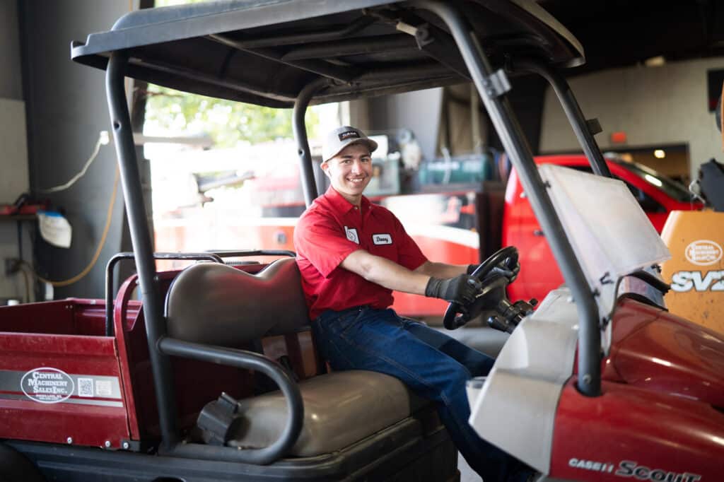 A young man in a red shirt sits behind the wheel of a golf cart-style buggy.