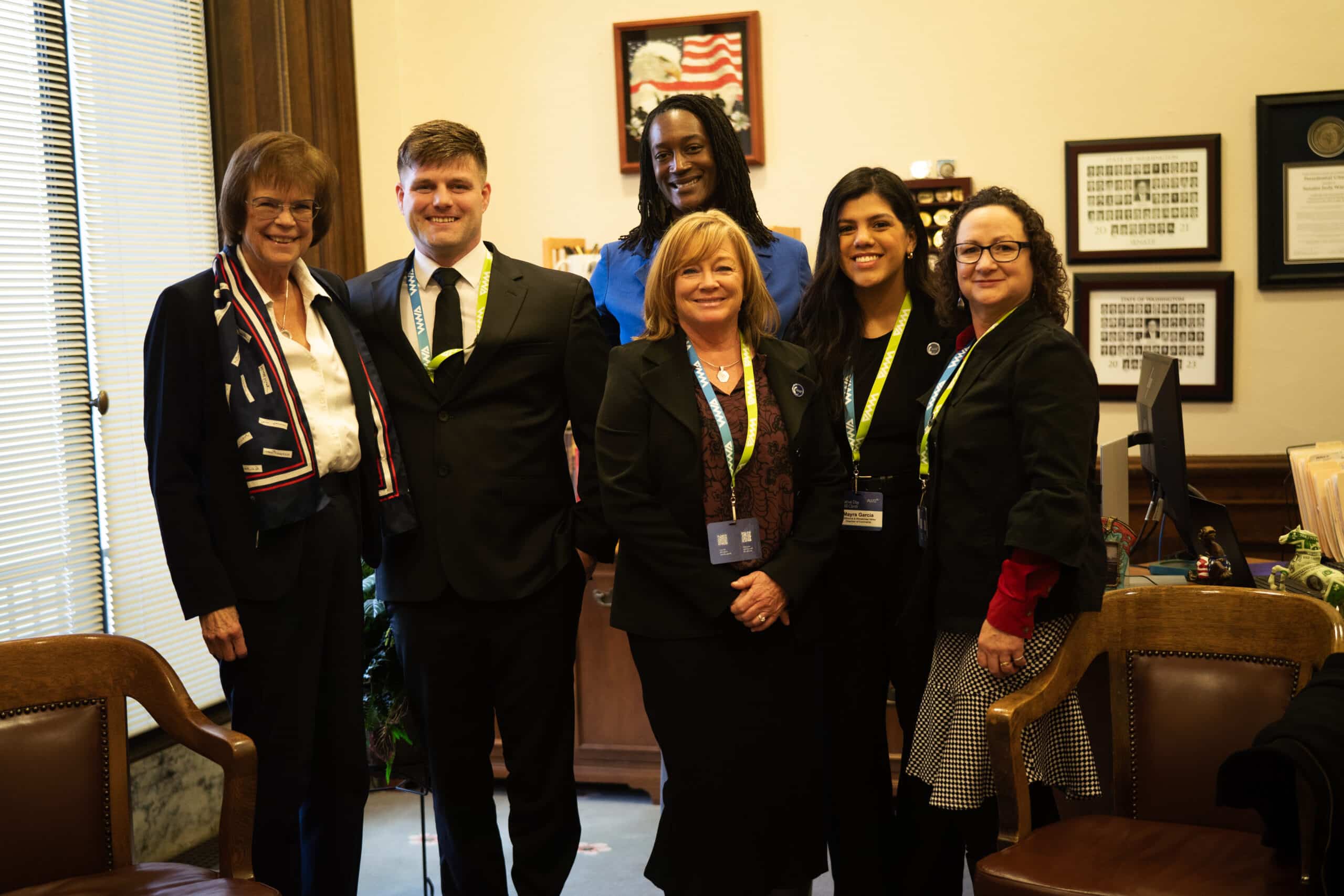 Six people in professional attire stand together with Senator Judy Warnick in her office at the Capitol.