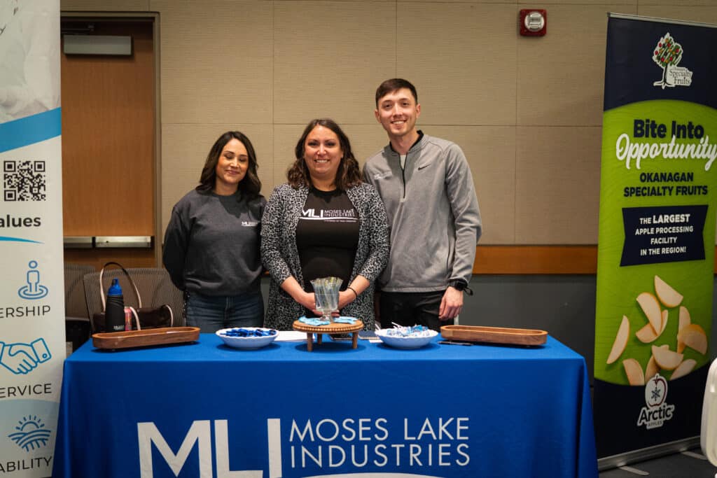 A group of 3 adults behind a booth at the job fair at Big Bend Community College