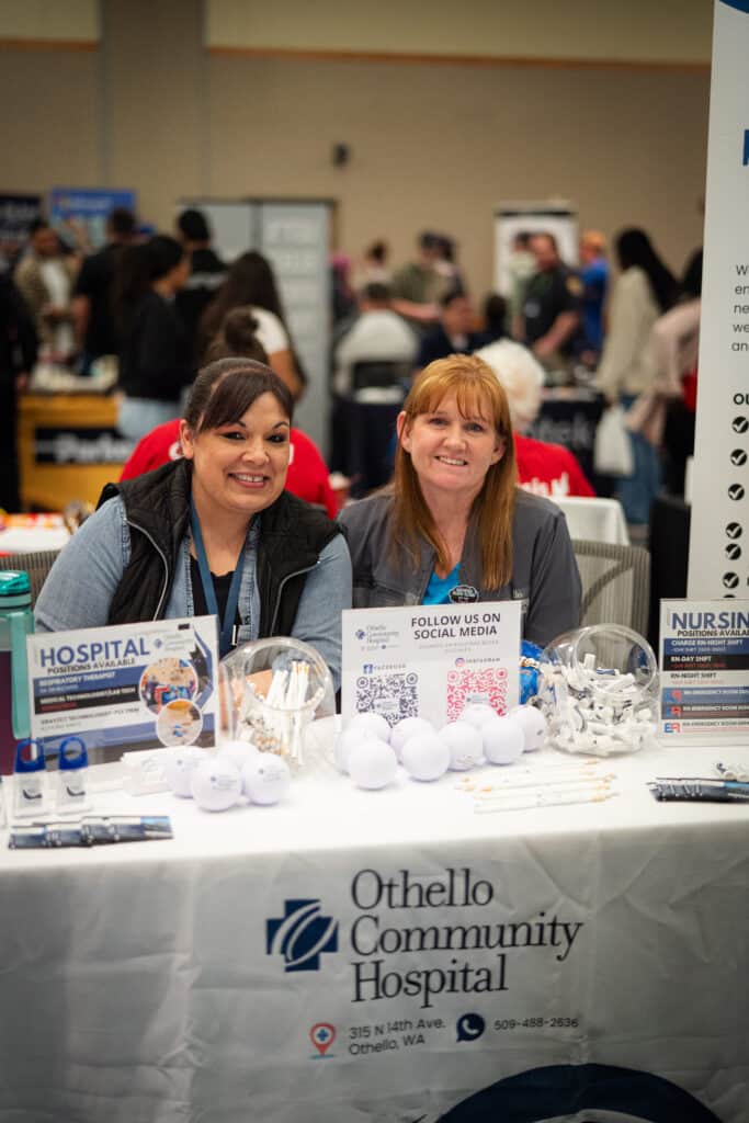 Two women sitting at a table smiling at the camera at Big Bend Community College&#039;s Job Fair