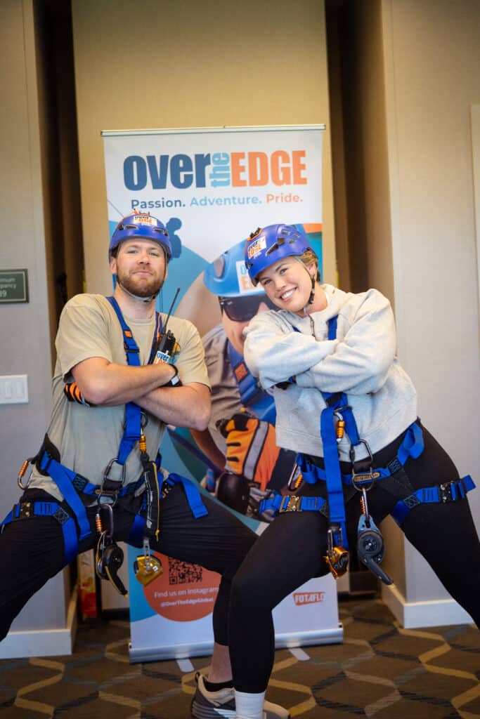 Two adults smiling at the camera ready to rappel off the Residence Inn Building