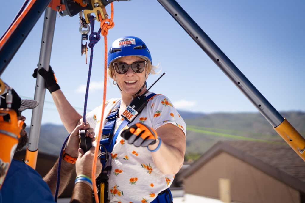 Woman smiling at the camera while her rope is getting adjusted in preparation to rappel off the Residence Inn Building