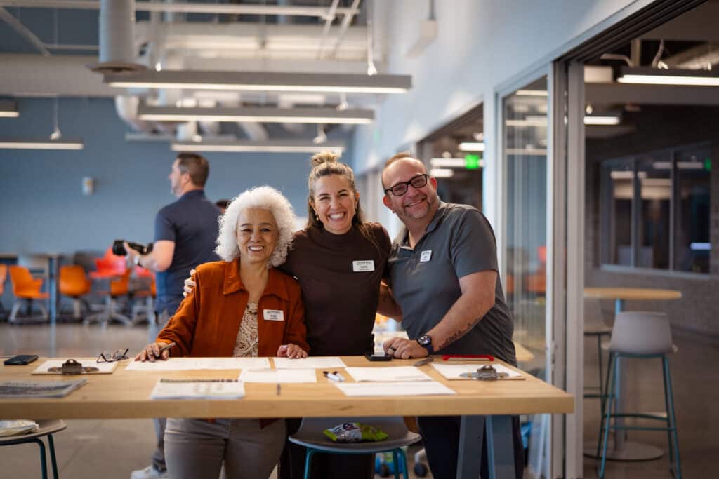 A group of 3 adults with big smiles leaning behind a table at Big Bend Community College.