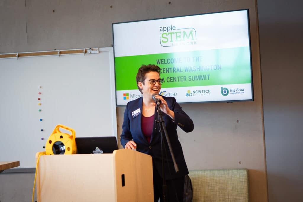 A lady smiling while doing a presentation in front of a room