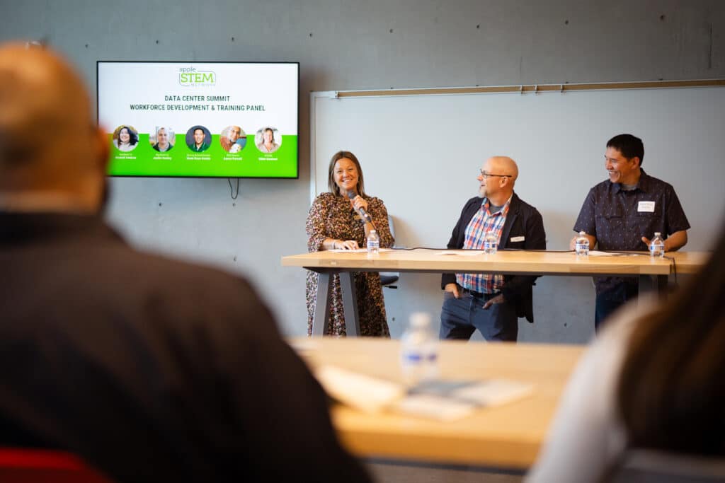 3 adults smiling while doing a presentation at Big Bend Community College. Woman to the left is holding a mic