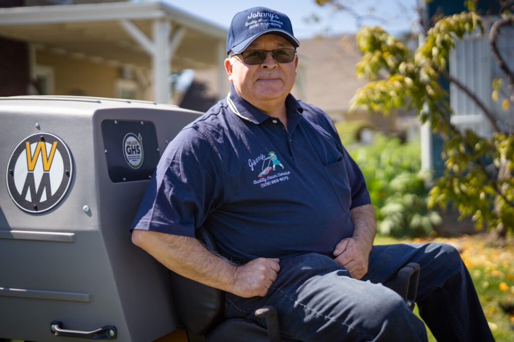 A gentleman with a navy blue hat and t-shirt sitting on a lawnmower looking at the camera