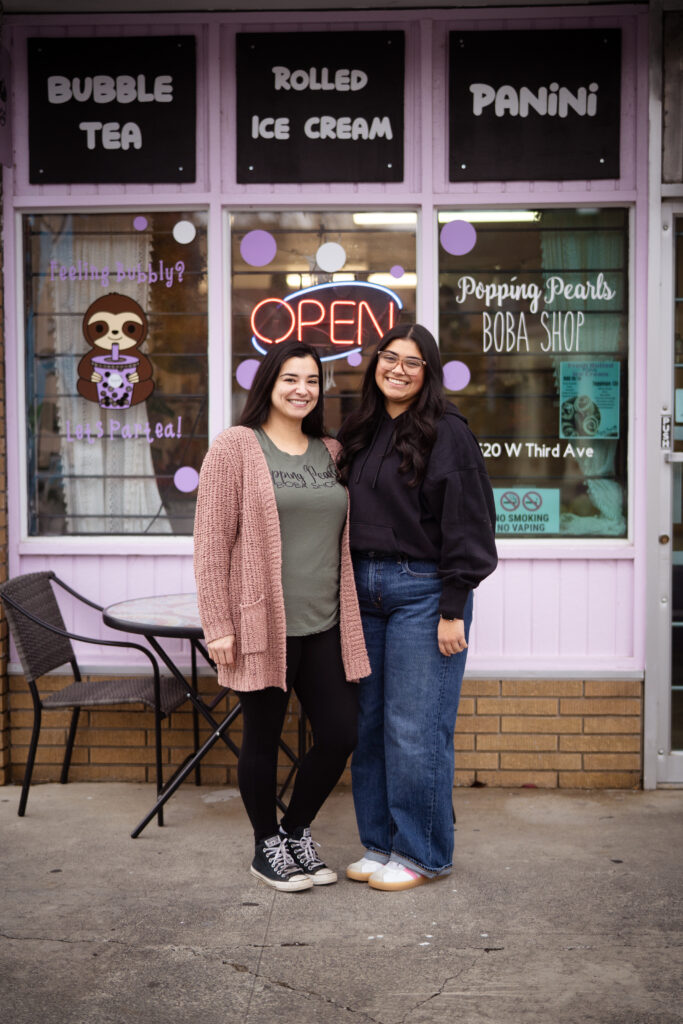 Two women with brunette hair standing Infront of their business Popping Pearls Boba Shop