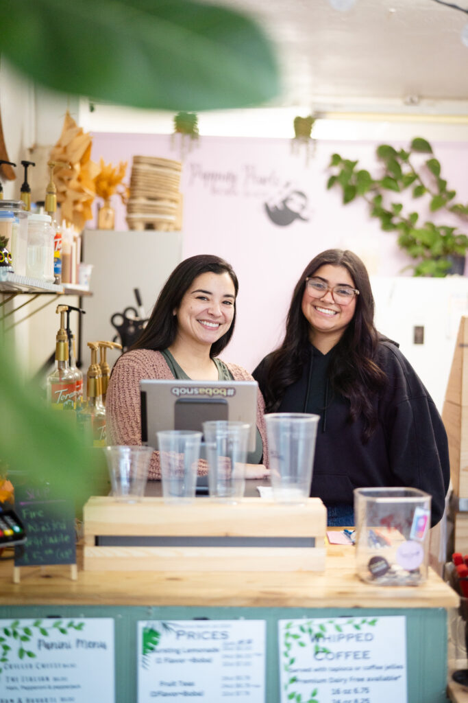 Two women with brunette hair standing behind a desk smiling at the camera