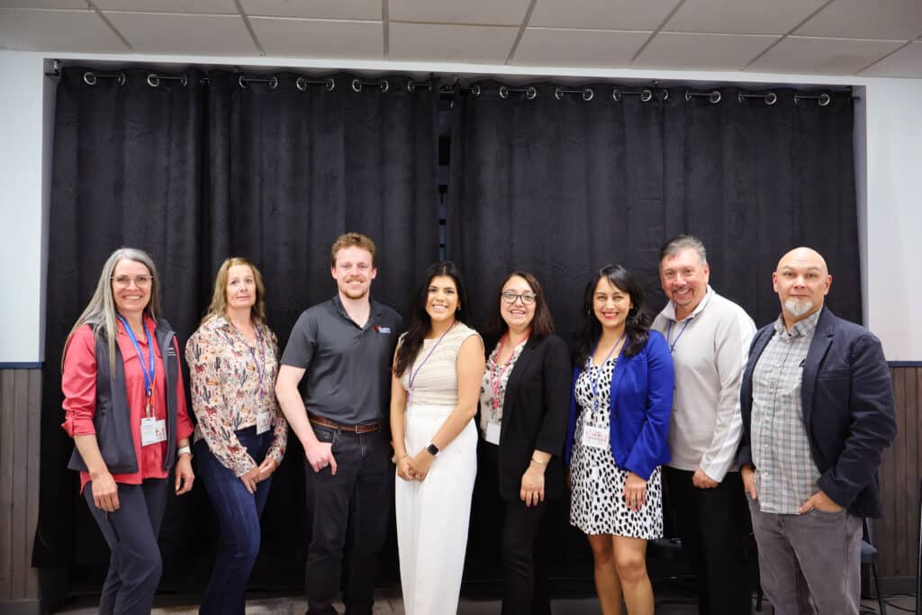 8 Workforce collaboration members standing in a straight line while smiling at the camera