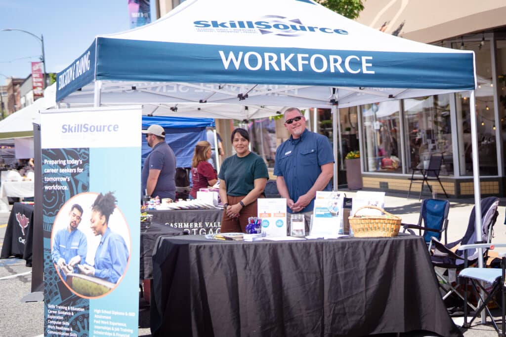 Two members of SkillSource staff standing behind an outdoor booth