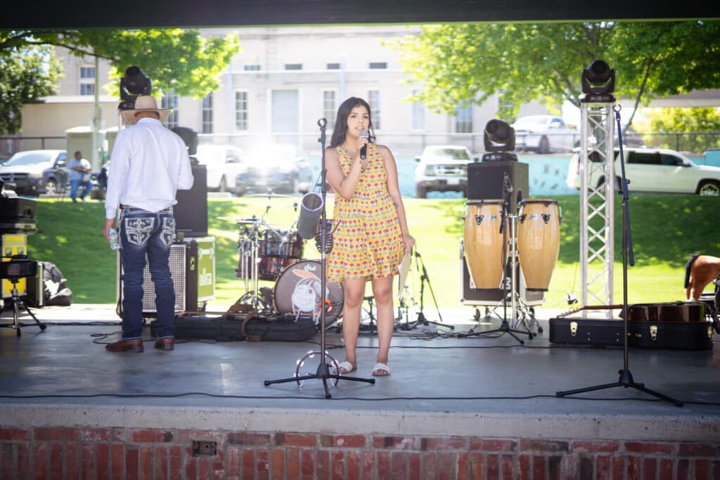 A woman wearing a yellow dress is on stage talking through a mic