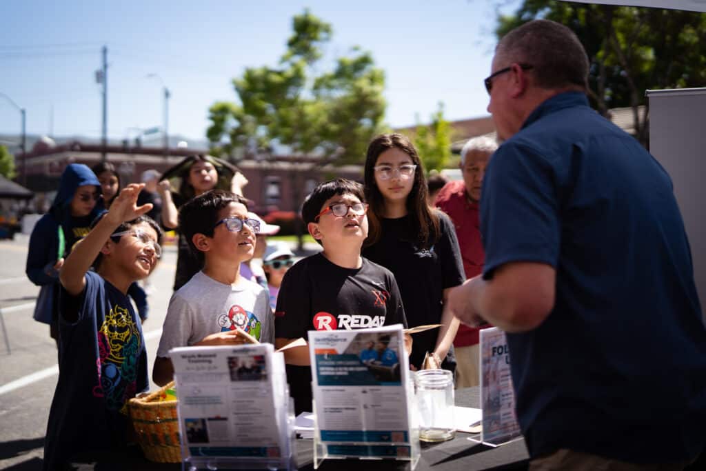 A group of children are talking to an adult at an outdoor booth
